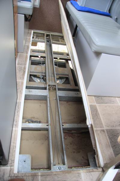 Dit is het inspektieluik in de caravan voor de hefkabels. 
Achterin het midden wordt door de lier een blok met vier kabels aangetrokken om het bovendeel omhoog te trekken. 
Twee kabels gaan via rollers halverwege naar de achterhoeken, en twee andere kabels via rollers vooraan naar de voorhoeken.